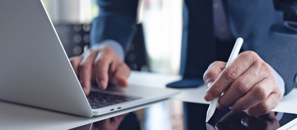 Una persona in giacca e cravatta sta digitando su un laptop e su in tablet